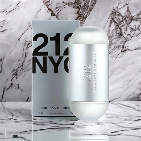 Frasco cilíndrico prata metálico do perfume feminino Carolina Herrera 212 NYC ao lado de sua caixa prata sobre superfície de mármore branco.
